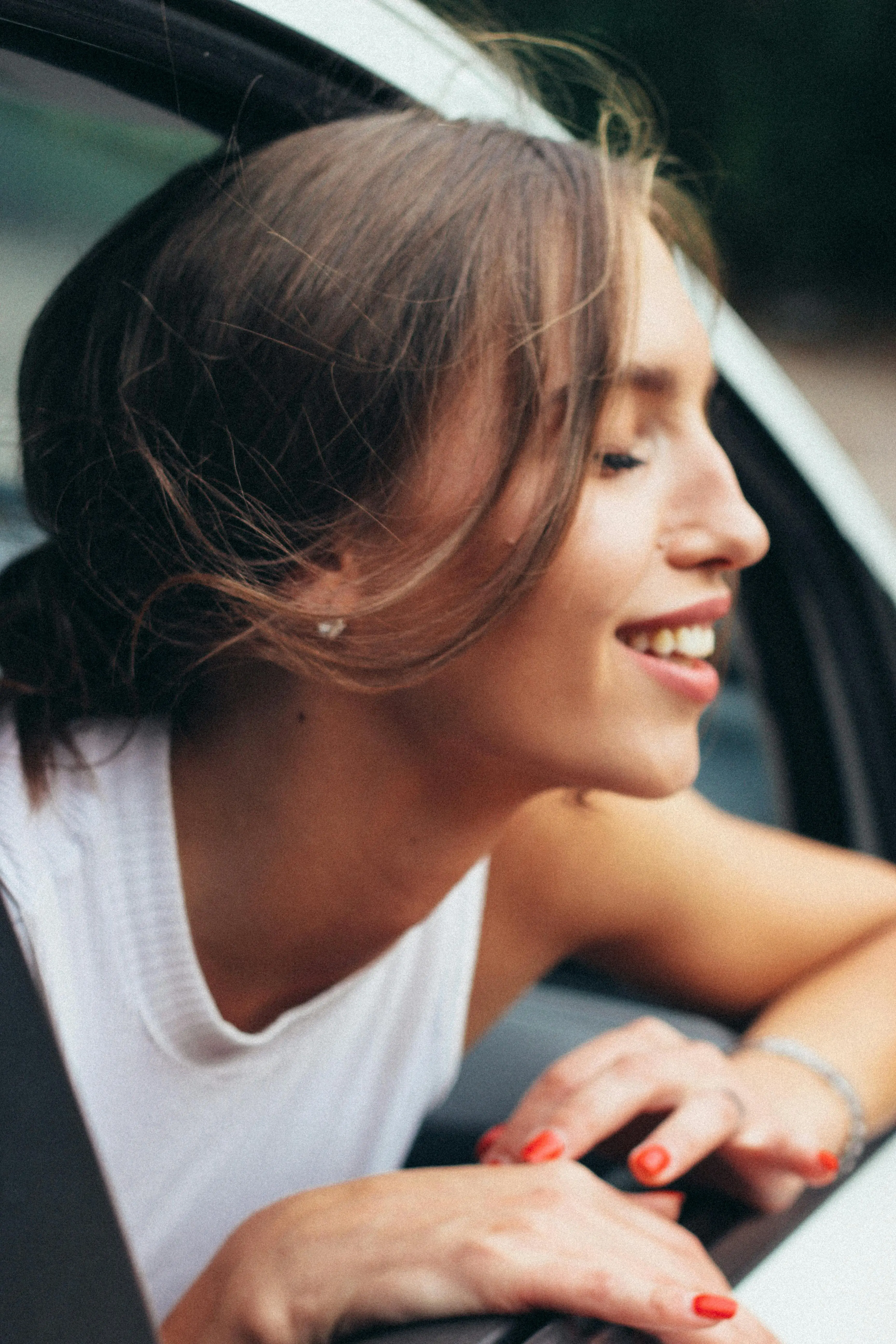 Mujer sonriente asomada por la ventana de auto. 